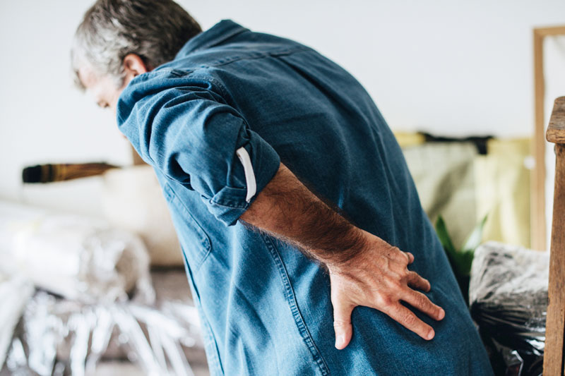 Older man is bent, holding his back because of chronic back pain