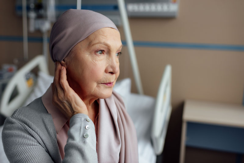 Woman looking solemn, experiencing cancer pain, wearing a hair wrap due to chemotherapy